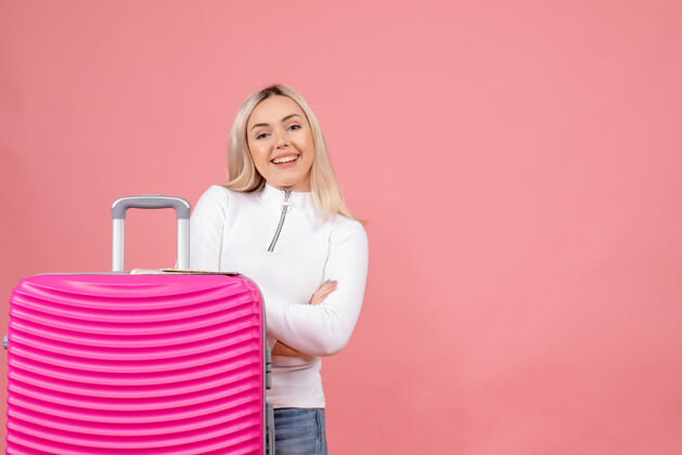 休闲正面图微笑的年轻女士站在粉红色的手提箱后面快乐前面站立