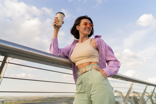 时尚幸福的女人 完美的身材 穿着时尚的紫色超大号衬衫 一边在摩登桥上享受着一杯咖啡肖像模特享受