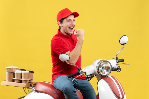 人一个穿着红色上衣 戴着帽子 在黄色背景下传递命令的快乐微笑的年轻人的正面视图黄色红色摩托车