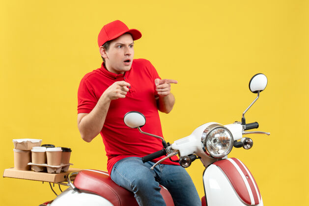 命令一个穿着红色上衣 戴着帽子 在黄色背景上向上传递命令的年轻人的正面照片年轻人交付摩托车