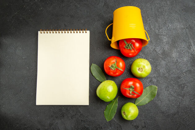 饮食顶视图桶与红色和绿色的西红柿月桂叶和笔记本在黑暗的背景素食叶子食物