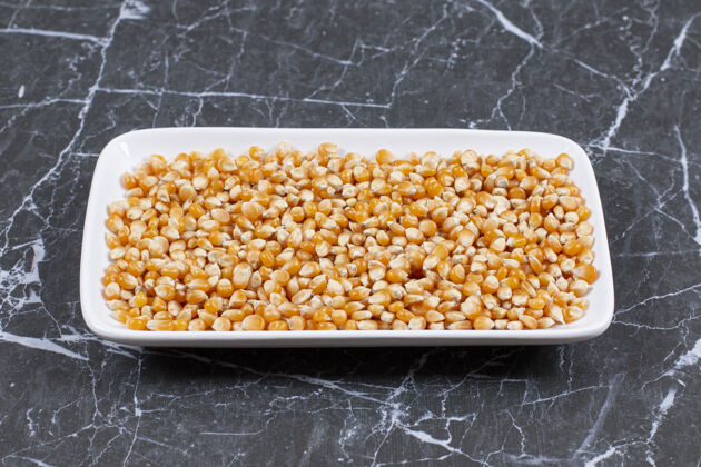 玉米把一堆新鲜的玉米种子放在黑盘子上的白盘子上谷物蔬菜堆
