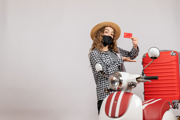 男人戴着黑色面具 手持旅行票 站在红色轻便摩托车旁的可爱小女孩的正面图服装剑旅行