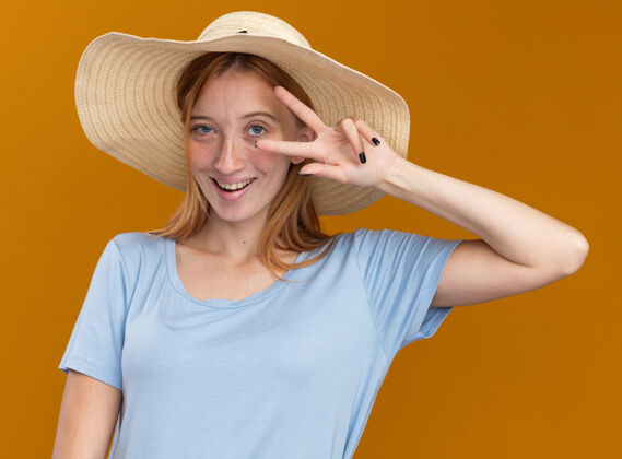 请高兴的年轻红发姜姑娘雀斑戴沙滩帽手势胜利标志橙色姜橙色标志