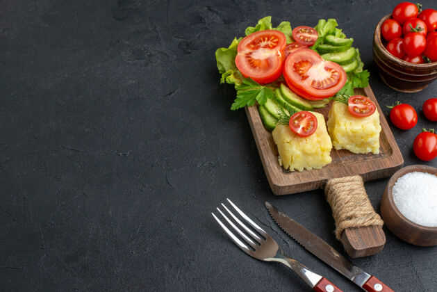 餐厅切好的新鲜西红柿和黄瓜的侧视图木板餐具上的奶酪在黑色表面的左侧放盐沙拉奶酪左