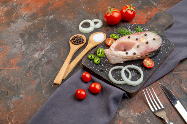 板侧视图生鱼和胡椒洋葱绿色西红柿在黑色切割板上毛巾餐具设置在混合颜色的表面毛巾美食膳食