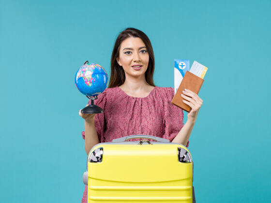 快乐前视女性在旅行中手持机票和地球仪在蓝色背景上女性旅行度假海上旅行地球仪人举行