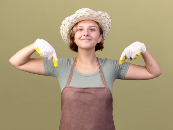 手套高兴的年轻斯拉夫女园丁戴着园艺帽和手套指着橄榄绿斯拉夫人指尖帽子