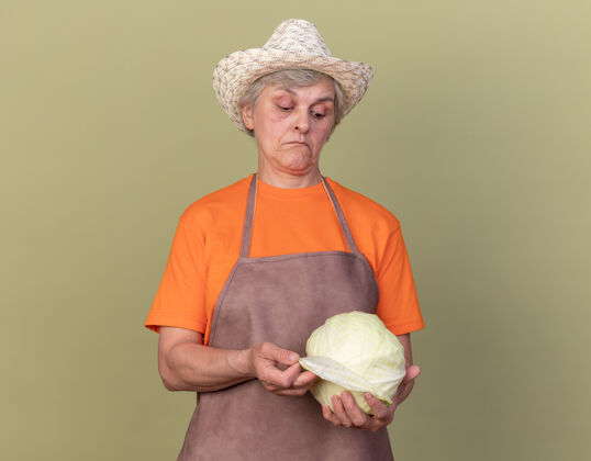 印象印象深刻的上了年纪的女园丁戴着园艺帽 拿着橄榄绿的卷心菜看着橄榄帽子卷心菜