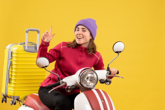 人正面图：坐在轻便摩托车上的快乐的年轻女子手指向上前面坐成人