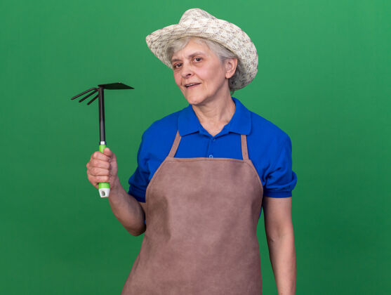 园艺自信的上了年纪的女园丁戴着园艺帽拿着锄头耙在草地上老人自信花园