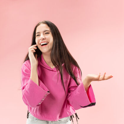 头发年轻漂亮的女人用手机演播室的粉红色演播室背景人类面部情感的概念流行的颜色通信持有漂亮