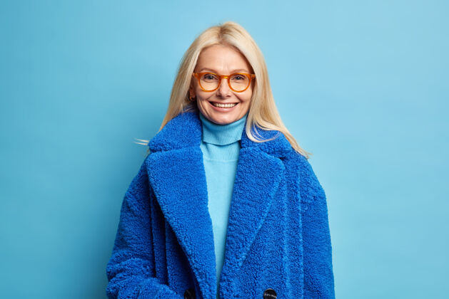 封闭微笑的欧洲女人 金发碧眼 穿着蓝色冬衣 心情愉快 戴着眼镜美丽外套穿着