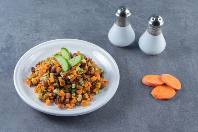 盐把蔬菜沙拉放在盘子里 旁边是胡萝卜片和盐放在大理石表面一餐黄瓜豆类