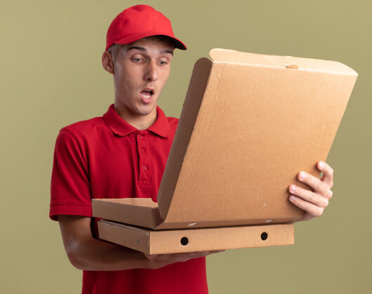 惊喜惊讶的年轻金发送货员抱着并看着橄榄绿上的比萨饼盒金发披萨年轻