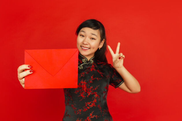旗袍2020年中国新年红色背景上孤立的亚洲少女肖像身着传统服装的女模特看起来很开心 微笑着 拿着红包庆祝 节日 情感女孩季节青少年