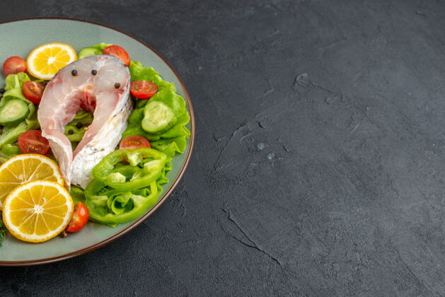 食物生鱼片和新鲜切碎蔬菜的俯视图柠檬片香料放在灰色盘子上 餐具放在黑色表面的右侧右侧生鱼餐具