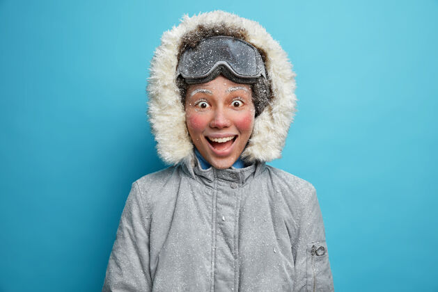 寒冷冬季运动和休闲活动概念快乐快乐活泼的女人 在暴风雪中冻红了脸 滑雪后很满意 穿着灰色夹克 在寒冷的日子里徒步旅行很有趣滑雪护目镜冰