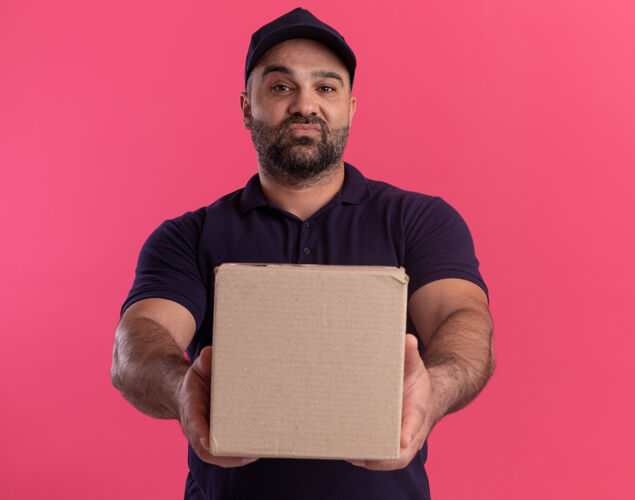 制服自信的中年送货员 穿着制服 戴着帽子 把箱子放在粉红色的墙上站着递送脸