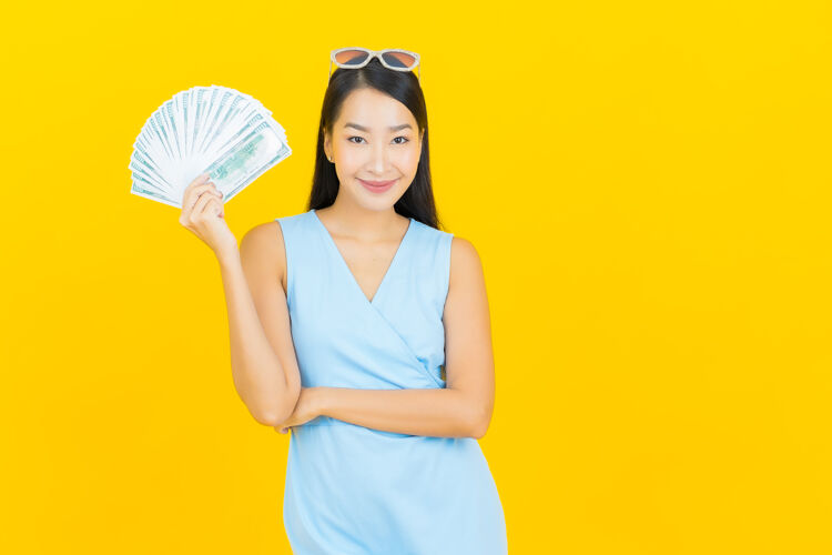 薪水肖像美丽的亚洲年轻女子微笑着在黄色的墙上有很多现金和金钱年轻付款钱