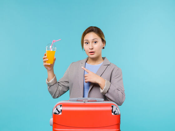 包正面图：度假中的女性 带着红色的袋子 拿着新鲜的果汁 在蓝色的背景下 度假飞机航行 海上旅行举行果汁前面
