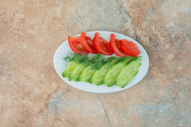 美味大理石桌上放着一个白盘子 上面放着黄瓜片和西红柿片食物蔬菜美味