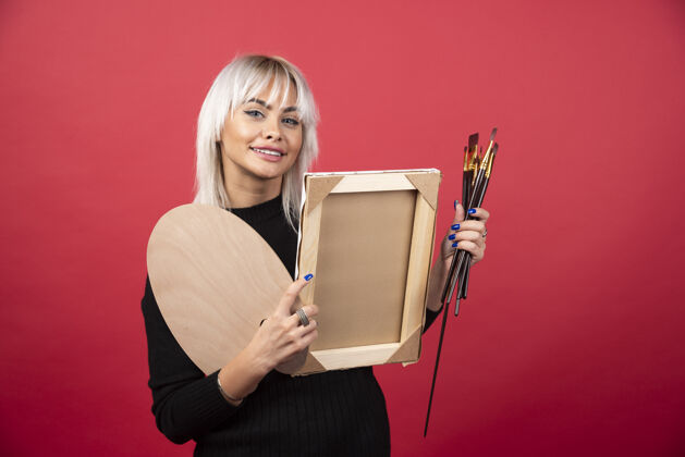 画笔年轻的女艺术家拿着艺术用品站在红墙上绘画调色板情感