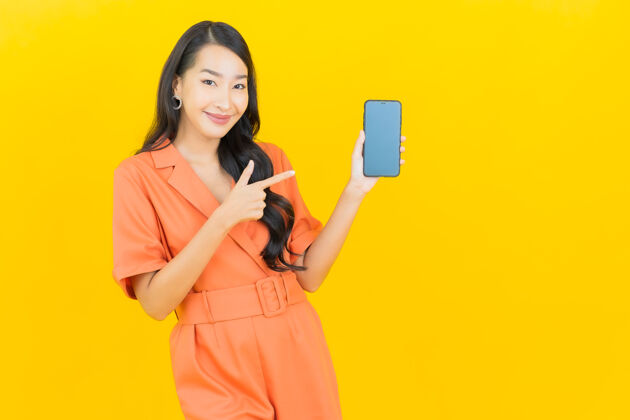 肖像肖像美丽的亚洲年轻女子微笑着智能手机上的黄色网络手机手持