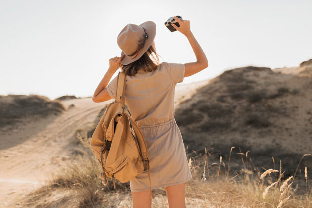 衣服沙漠中穿着卡其色长裙的迷人时尚年轻女子 在非洲旅行 戴着帽子和背包 用老式相机拍照人模型旅游