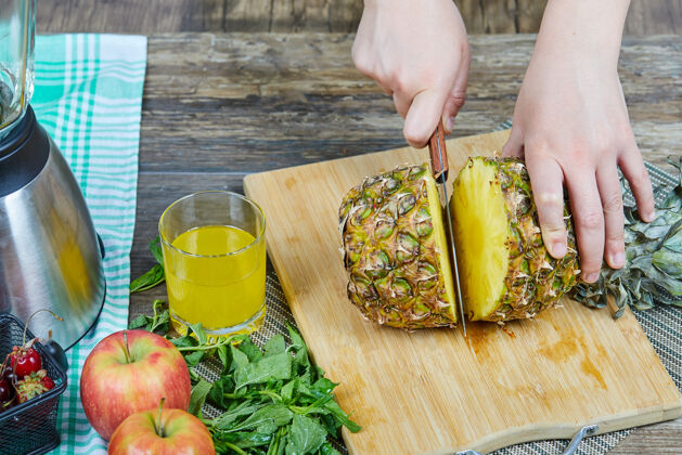 苹果一个女人在一块木板上切一个新鲜的菠萝 旁边放着苹果 蔬菜和一杯果汁颜色切黄色