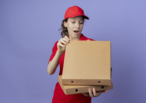 送货令人印象深刻的年轻漂亮的送货女孩穿着红色制服和帽子举行比萨饼包 并期待在紫色背景与复制空间隔离包内印象漂亮包装