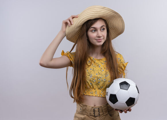 足球自信的年轻女孩戴着帽子拿着足球 把手放在帽子上孤立的白色空间抱着戴着自信