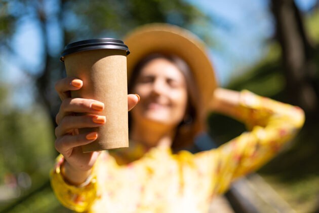 20多岁穿着黄色夏装 戴着帽子 在公园里喝着咖啡的女人的户外肖像女性欢乐茶