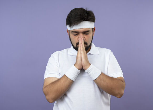 运动年轻的运动型男子 戴着头带和腕带 闭着眼睛 表现出祈祷的姿态人关闭头带