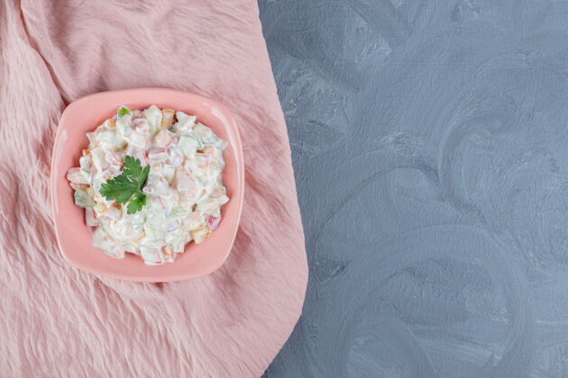 美味一碗奥利弗色拉 在大理石桌上的粉色桌布上点缀着欧芹叶美味欧芹装饰
