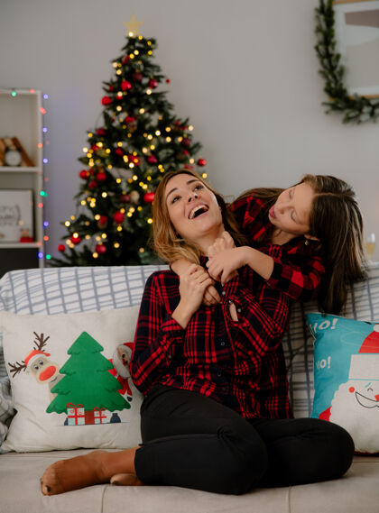 舌头快乐的女儿结结巴巴地吐出舌头 拥抱坐在沙发上的母亲 在家里享受圣诞节时光圣诞节拥抱时间