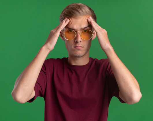 人自信的年轻帅哥穿着红衬衫戴着眼镜把双手放在额头上隔离在绿色的墙上眼镜自信公民