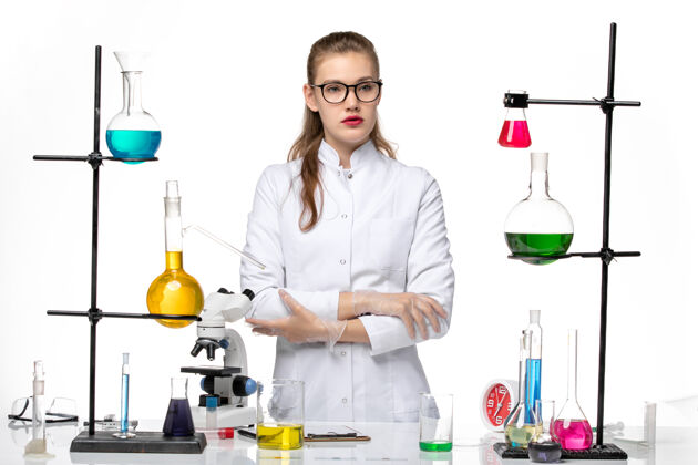 桌子前视图身着医疗服的女化学家在白色办公桌上遥望远方化学病毒大流行病毒医生人严肃