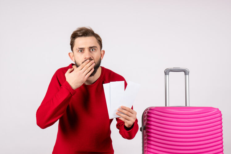 度假正面图：年轻男性 带着粉色包 手持白墙彩色旅行票 度假航班 暑期旅游者肖像颜色年轻男性
