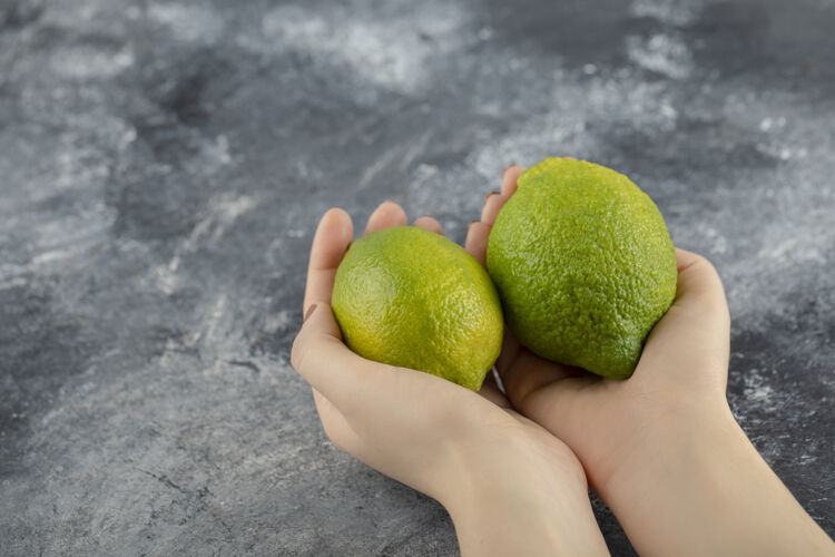 热带女人手里拿着两个新鲜的绿色柠檬自然持有美味