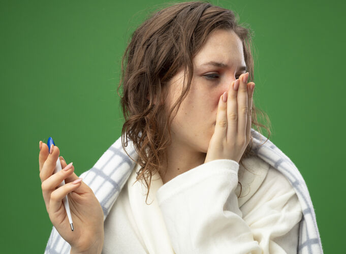 抱着虚弱的年轻病女孩穿着白袍裹着格子布拿着温度计捂着嘴用手隔离在绿色上格子虚弱嘴巴