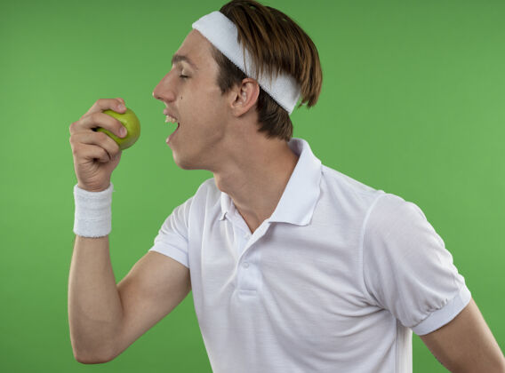 个人站在侧视图年轻的运动男子戴着头带与腕带咬苹果苹果运动观点