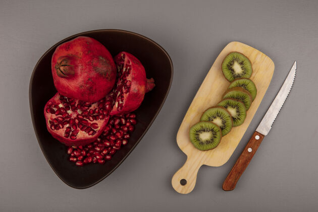 碗顶视图新鲜的一半和整个石榴在一个碗与切片的猕猴桃在一个木制的菜板与刀石榴食物板