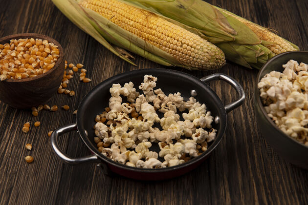 电影顶视图锅爆米花与玉米粒与新鲜的玉米隔离在一个木碗在一个木桌上木材观点顶部