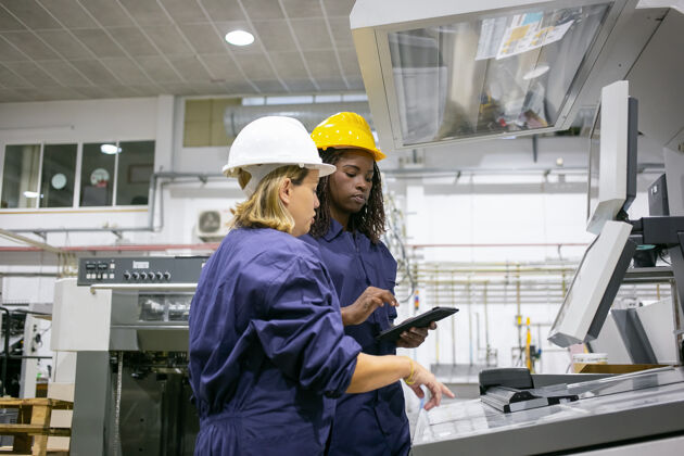 技术女工业员工教同事操作机器 指着控制板 用平板电脑技师工厂制造