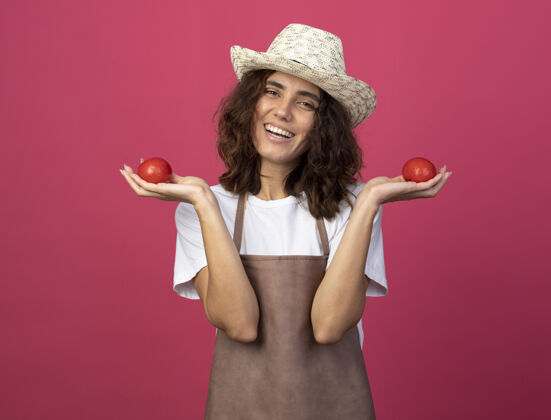 年轻微笑着的年轻女园丁穿着制服 戴着园艺帽 手里拿着西红柿成年人快乐人