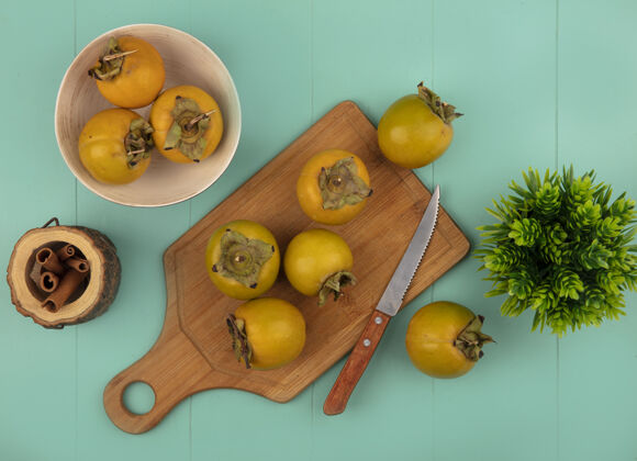 水果顶视图橙色圆润柿子水果在一个木制厨房板与刀肉桂棒在一个蓝色木桌上的木罐罐子观点木板