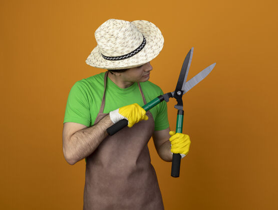 思想一个穿着制服 戴着园艺帽 戴着手套的沉思的年轻男园丁 手里拿着一把剪子 看着橘子上孤立的剪子剪子男穿