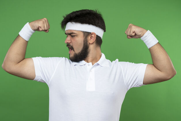 穿自信的年轻人戴着头带和腕带 在绿色上显示出强烈的姿态强壮自信腕带