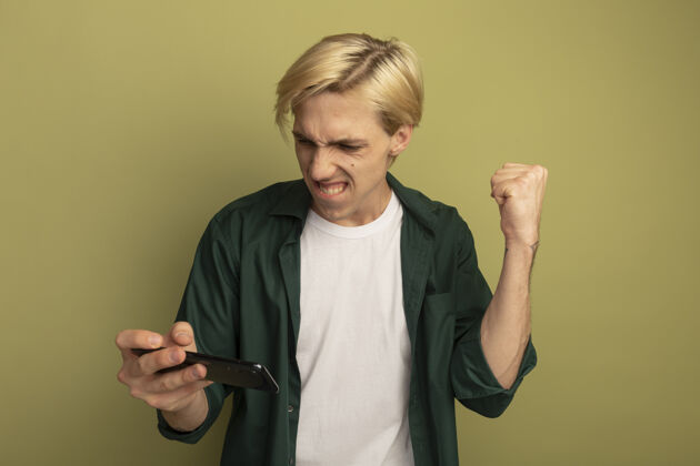 男人兴奋的金发小伙子穿着绿色t恤拿着手机 看着手机 表示同意穿秀人